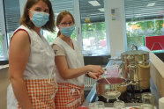 Zwei Frauen mit Mund-Nasen-Bedeckung stehen vor Kochfeld in Lehrküche