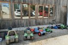 Mehrere Kinderfahrzeuge stehen vor Holzwand. In den Fenstern spiegeln sich Autos.