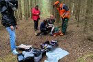 Frau schminkt Bein von Mann. Mehrere Personen stehen um sie herum.