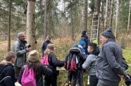 Kinder, Begleiter und Förster stehen vor Baum mit Nistkasten.