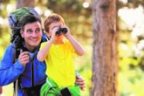 Vater und Sohn spazieren im Wald. Der Sohn hält ein Fernglas vor seine Augen.