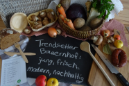 Beschriebene Tafel auf tisch, daneben Kochlöffel, Zwiebeln, Karotten und Äpfel