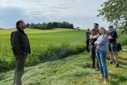 Menschen stehen auf frisch gemähter Wiese. Im Hintergrund Büsche und Hecken.