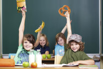 4 Kinder sitzen an Tischen und halten jeweils Breze, Banane und Papiergesicht in die Höhe © Christian Schwier – stock.adobe.com